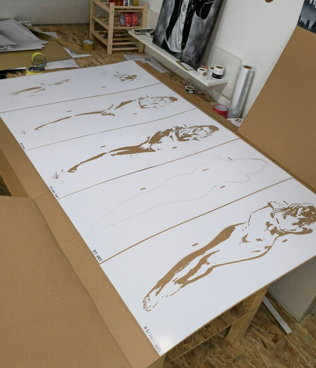 Multiple prints of a nude figure on white paper arranged on a table.